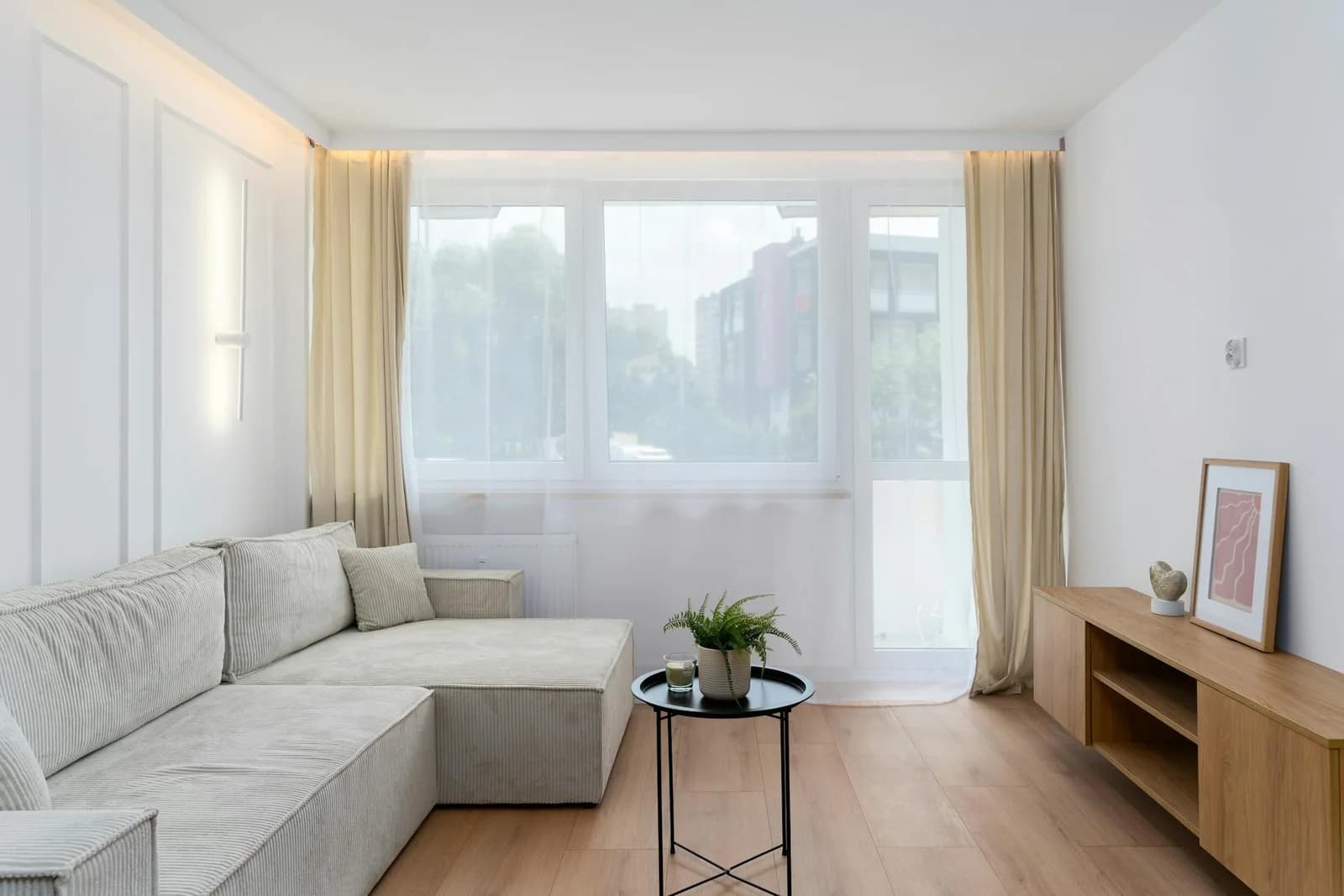 Salon scandinave lumineux avec canapé crème, rideaux beiges, bois clair et grande fenêtre baignée de lumière naturelle